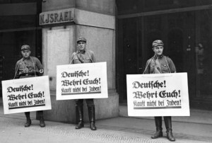 Members of the Nazi Sturmabteilung, the storm troopers, holding placards that say, "Deutsche! Wehrt Euch! Kauft nicht bei Juden!" or "Germans! Defend yourselves! Don't buy from Jews," in front of Israel's Department Store, in Berlin, on April 1, 1933, at the start of the Nazi boycott of Jewish-owned businesses. Photo: WikiCommons.