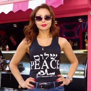 Moroccan journalist Ghislaine Taibi, wearing a Chai necklace and a Shalom tank top in front of a Jerusalem cafe. Photo: Screenshot.