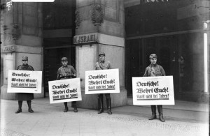 Nazi SA paramilitaries outside a Jewish-owned department store in Berlin. The signs read: "Germans defend yourselves! Don't buy from Jews." Photo: Wikipedia.