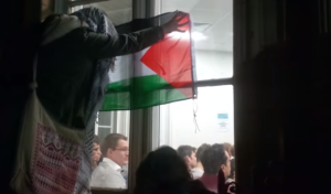 An anti-Israel protester with a Palestinian flag, outside the room where Ami Ayalon was giving a talk at Kings College London. The university concluded that the protesters "crossed the line." Photo: Youtube/Screenshot.