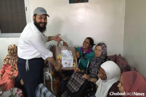 Rabbi Levi Banon of Jeunesse Chabad Morocco, center, handing food packages to needy Muslims. He led a group of volunteers to hand out the food bags. Photo: Chabad.org. 