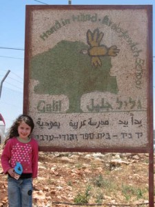 A young girl poses in front of the sign for the Galil Jewish–Arab School in northern Israel. Photo: JNS.org. 